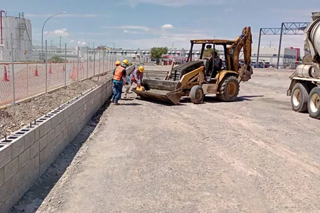 Cuadrilla y retroexcavadora construyendo la barda perimetral de la planta Cummins