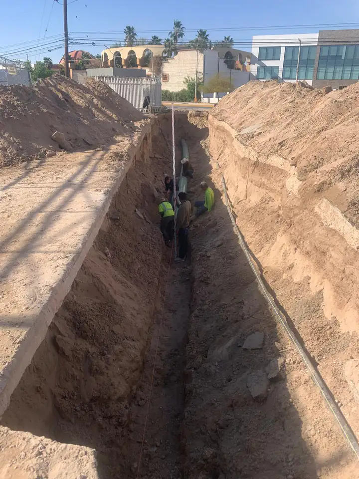 Cuadrilla trabajando en el fondo de la zanja con la mira topográfica para dar el nivel