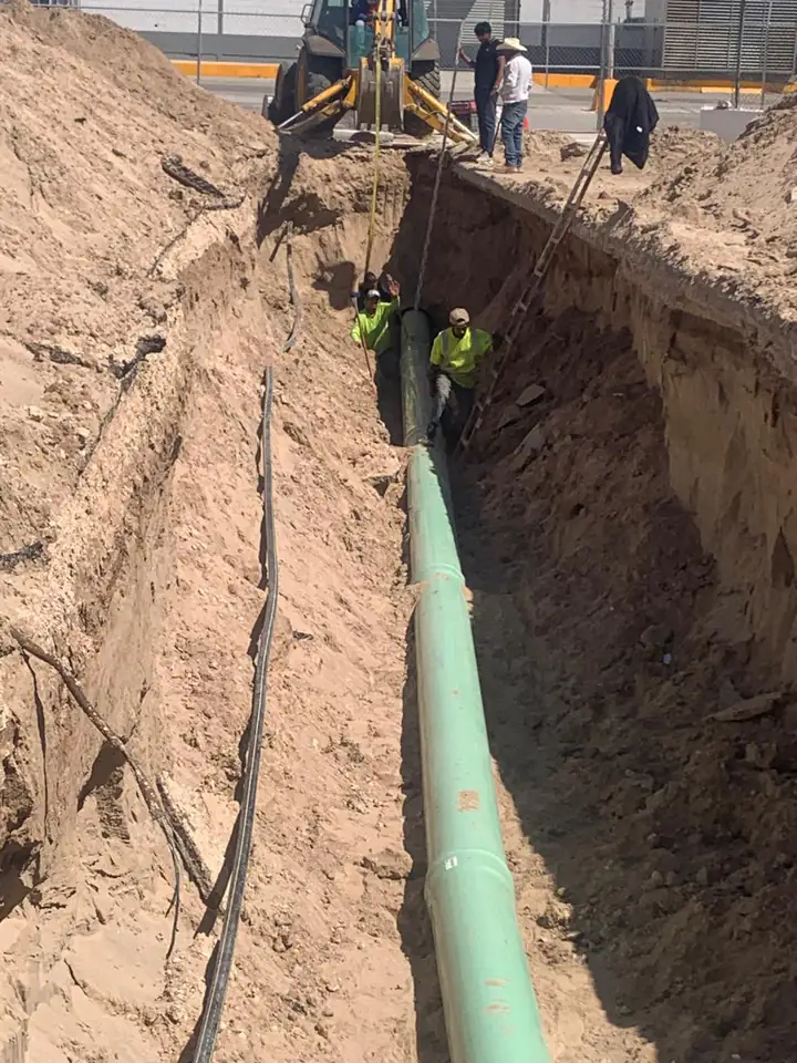 Tramo largo de la línea ya colocado en el fondo de la zanja, con escalera de acceso y retroexcavadora